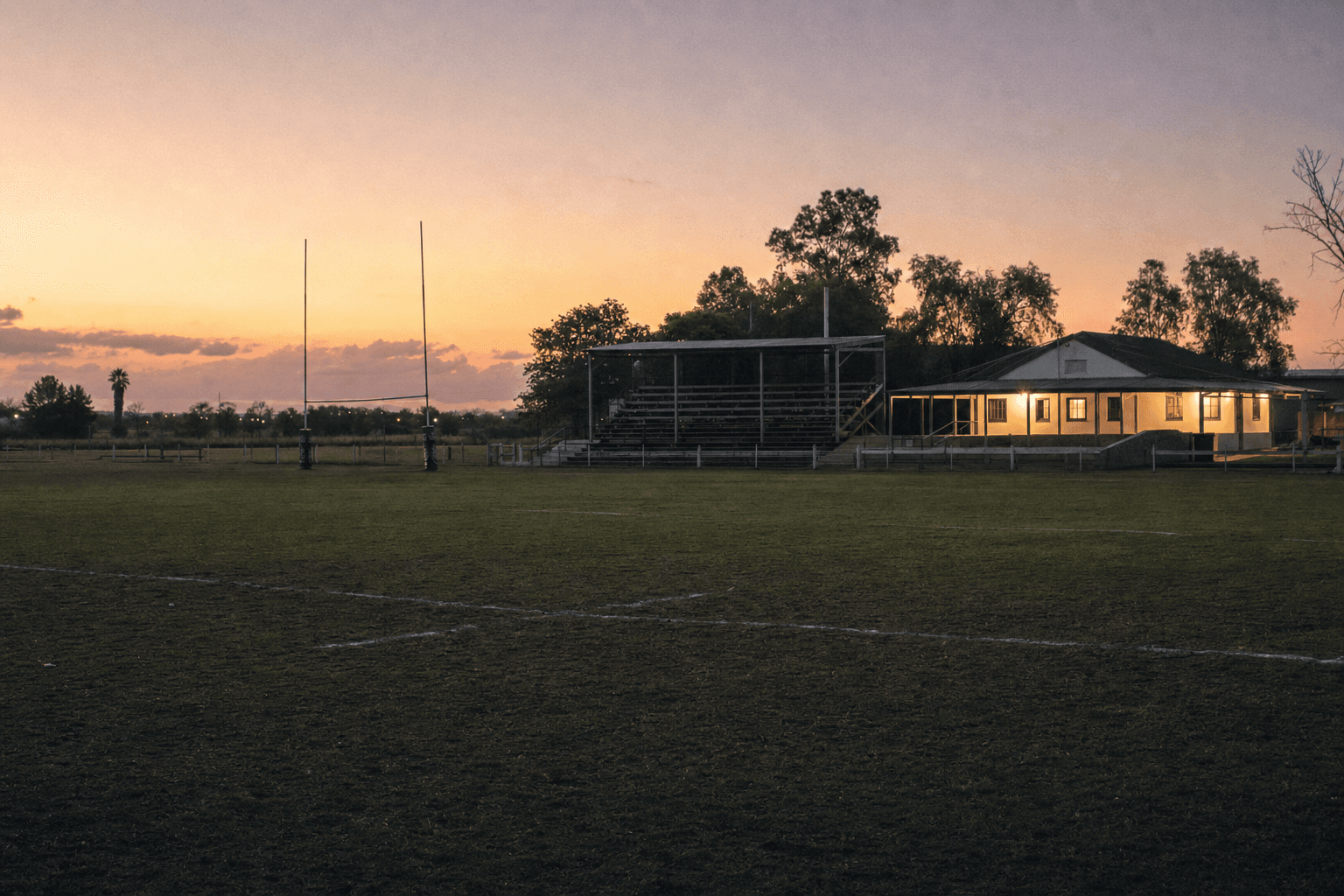 Cancha de un club de rugby amateur con su tribuna de madera al atardecer